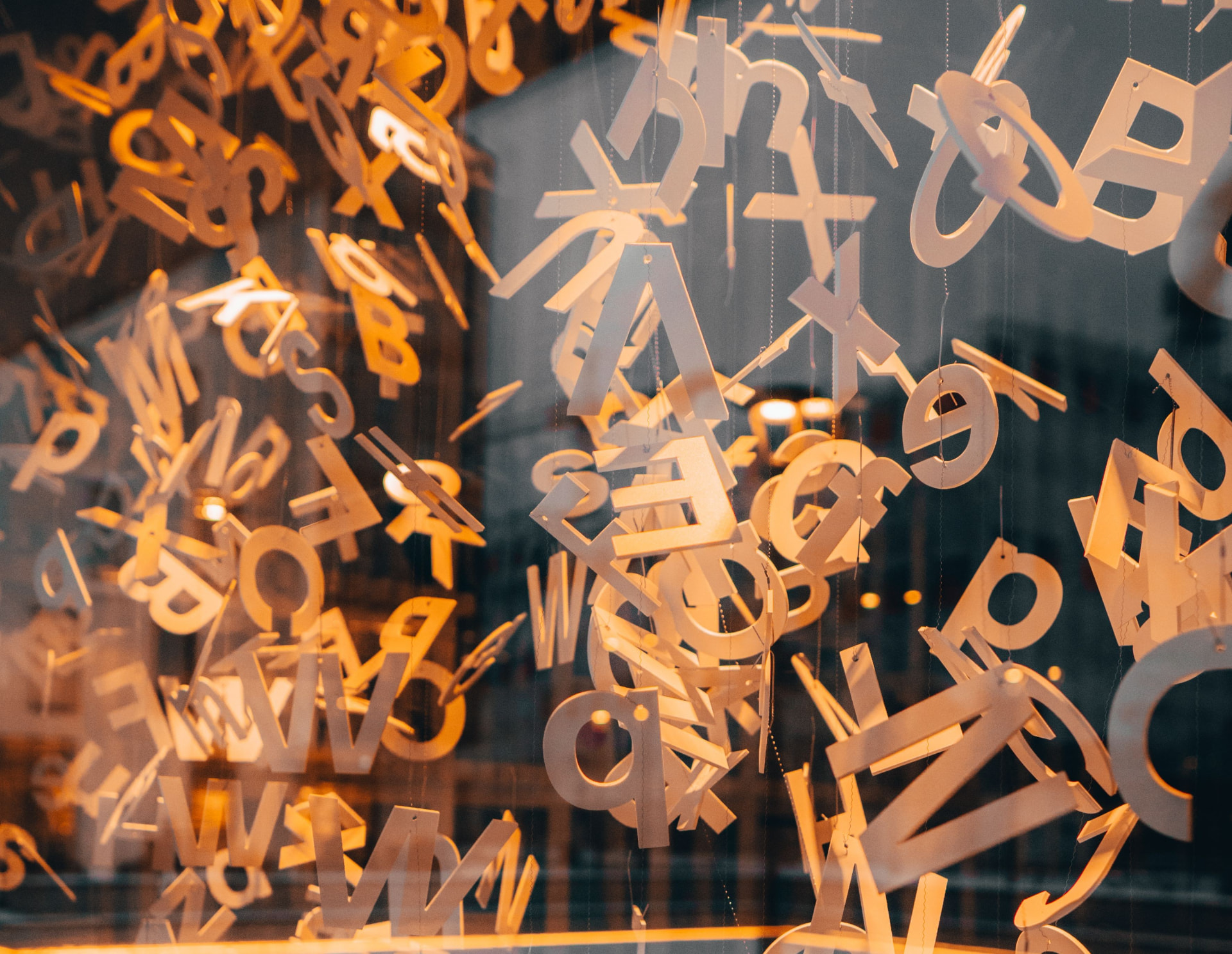 Dozens of metal letters hanging on threads in a warmly lit shop window